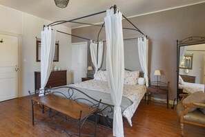 A four-poster canopy bed with a wooden table and chairs in a room with a wooden floor.
