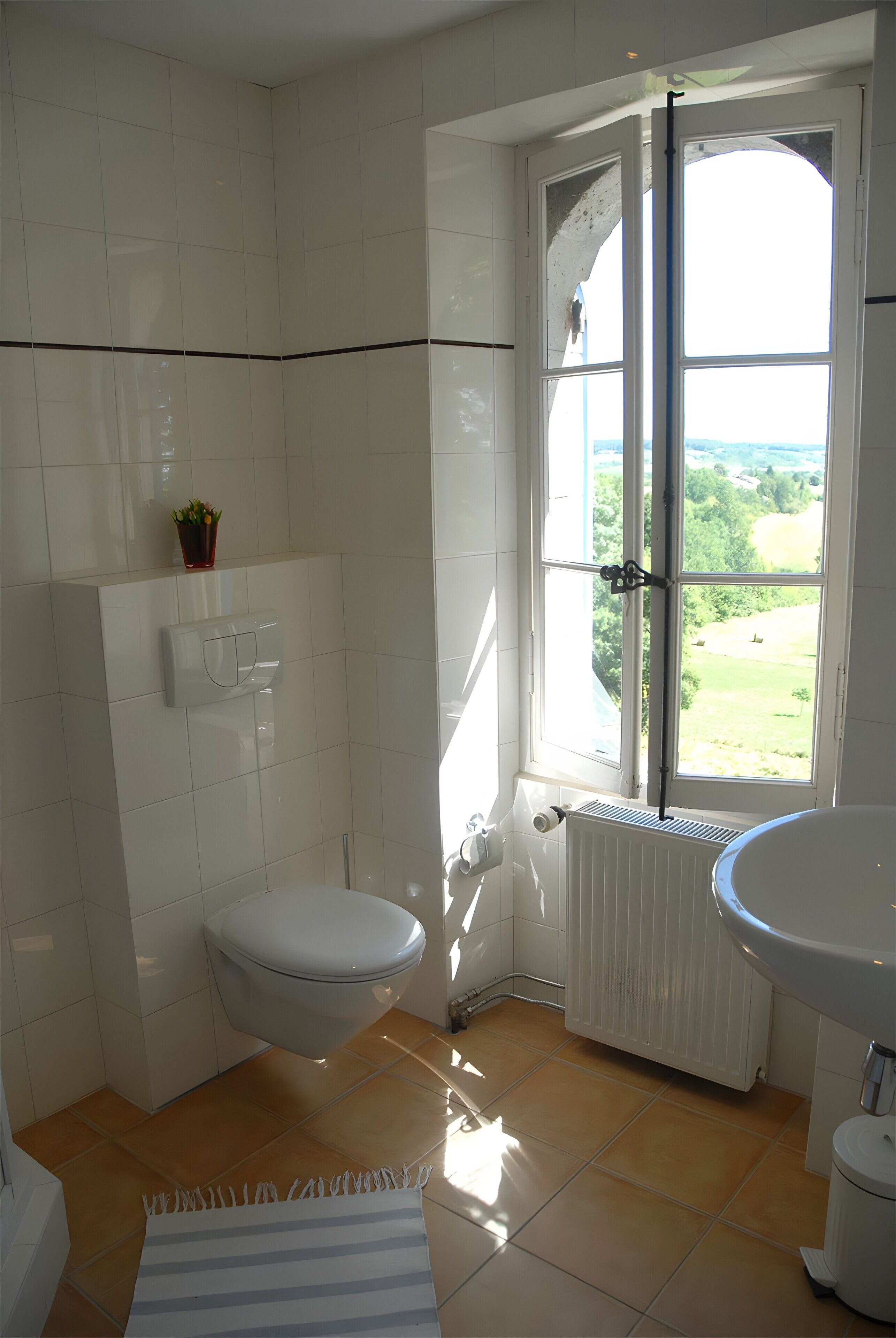 Ein Badezimmer mit Toilette, Waschbecken und einem Fenster mit Blick auf Grünflächen.
