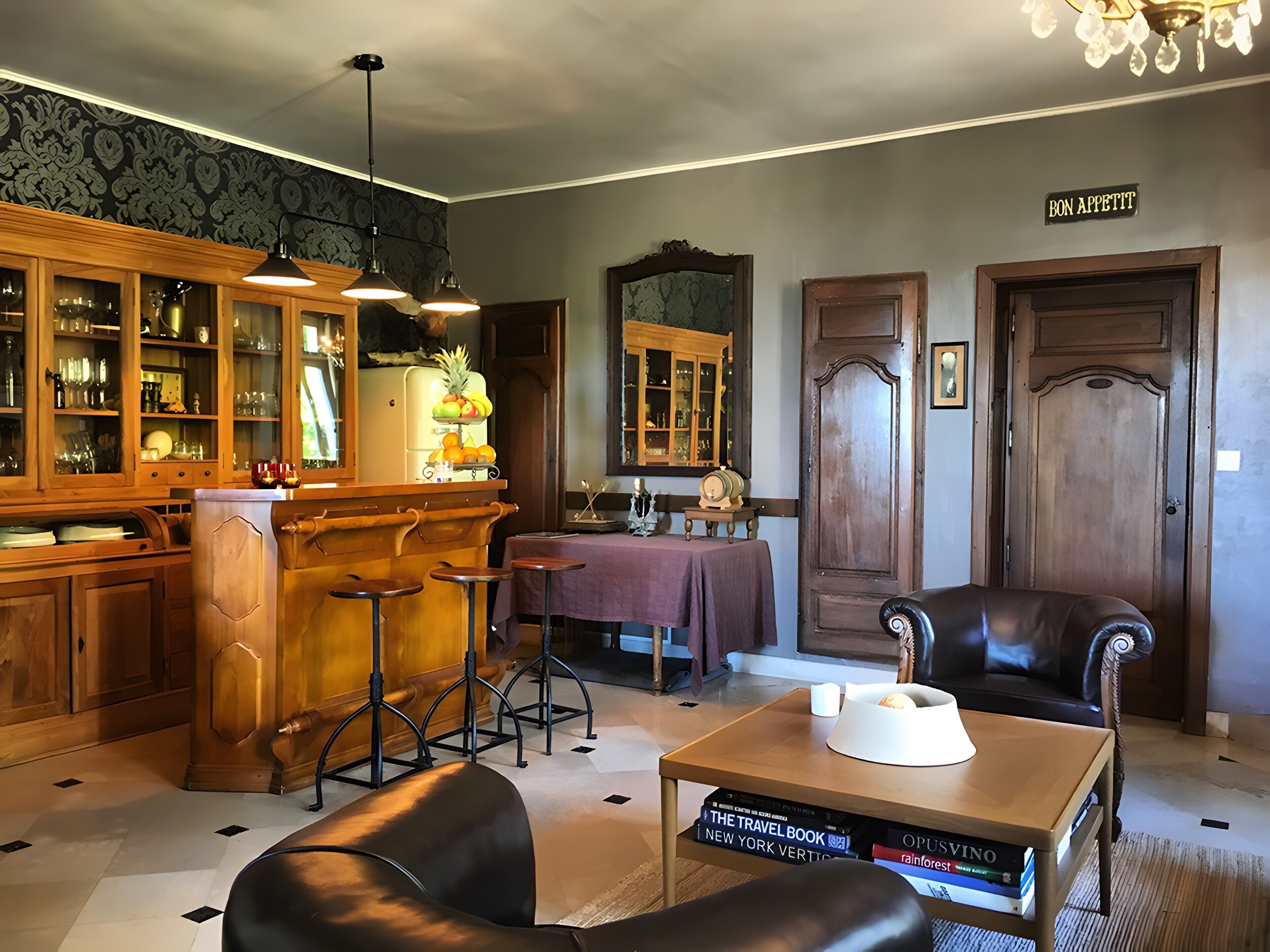 Um quarto com área de bar, armários de madeira, uma mesa de jantar e poltronas de couro.
