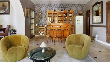 Una sala de estar con dos sillones, una mesa de centro de vidrio, un mueble de madera con puertas de cristal y un refrigerador blanco.