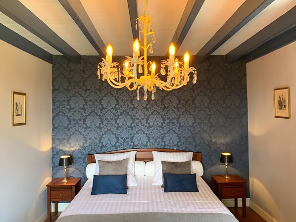 A hotel room with a large bed, two bedside tables, a chandelier, and patterned wallpaper.