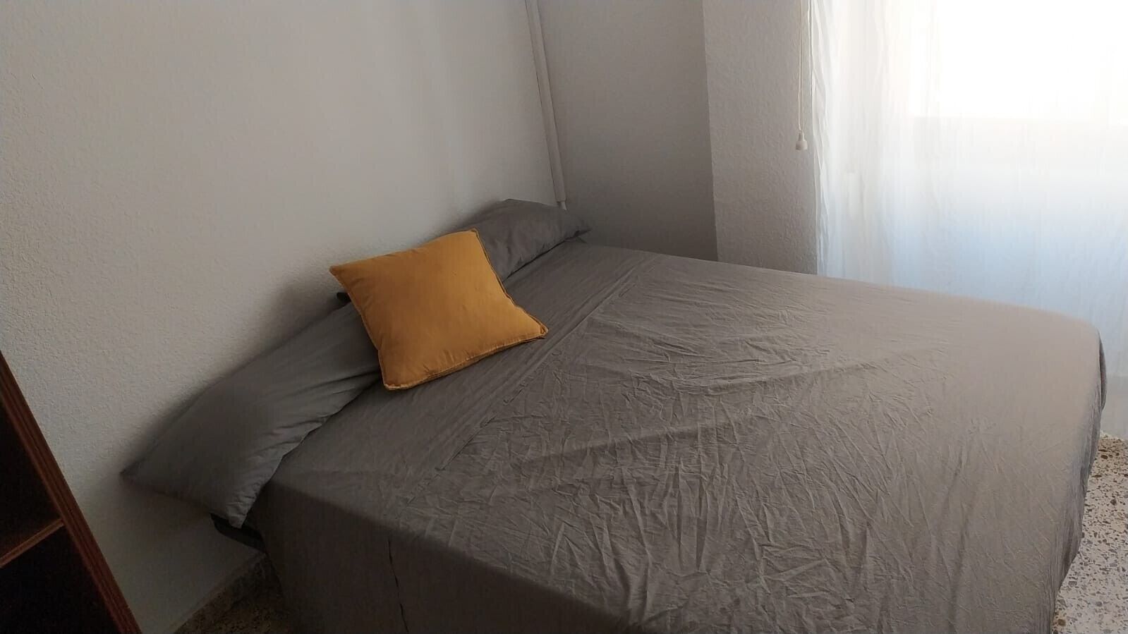 Ein Schlafzimmer mit einem Bett, einem Kopfkissen und einem Fenster mit Vorhängen.