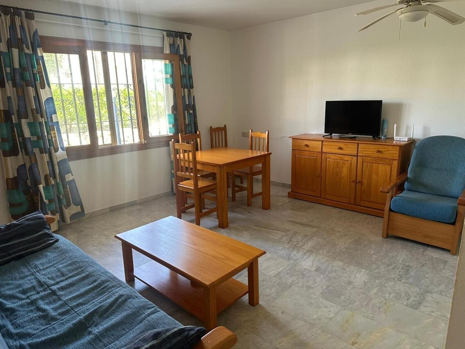 Una habitación con una mesa de comedor de madera, sillas, un televisor sobre un mueble de madera, un sillón azul y un sofá.