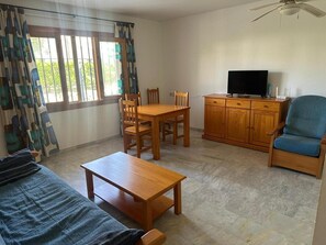 A room with a wooden dining table, chairs, a television on a wooden cabinet, a blue armchair, and a sofa. - Vera Playa Apartment with Communal Pool, Wi-Fi, and Air Conditioning (Las Marinas)