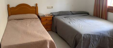 A bedroom with two beds, a nightstand, a lamp, and a window with curtains.