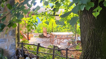 A rustic outdoor seating area with a wooden table and chairs, surrounded by greenery and a stone wall.