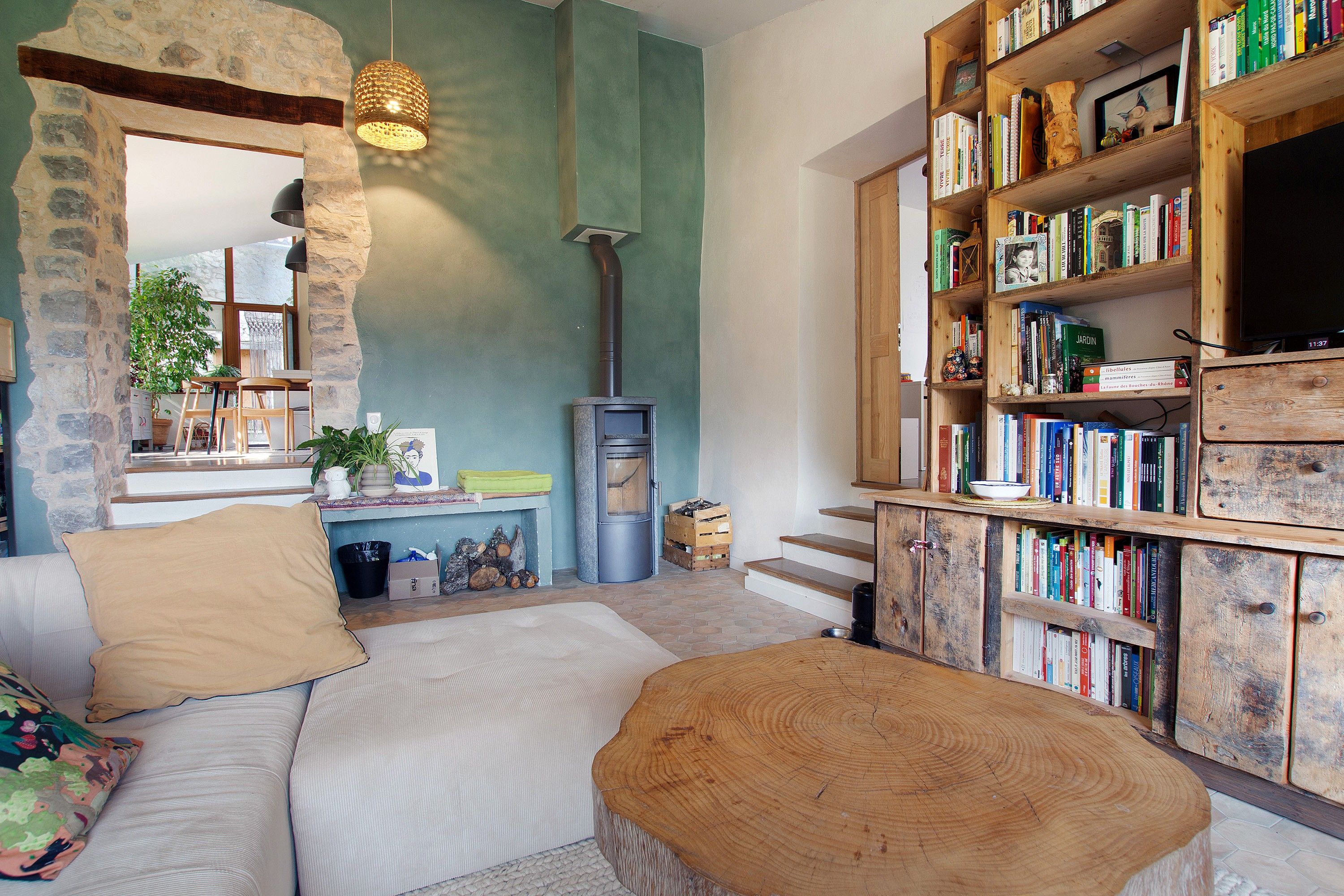 A cozy living room with a stone wall, a fireplace, a bookshelf, and a comfortable seating area.
