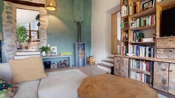 A cozy living room with a stone wall, a fireplace, a bookshelf, and a comfortable seating area.