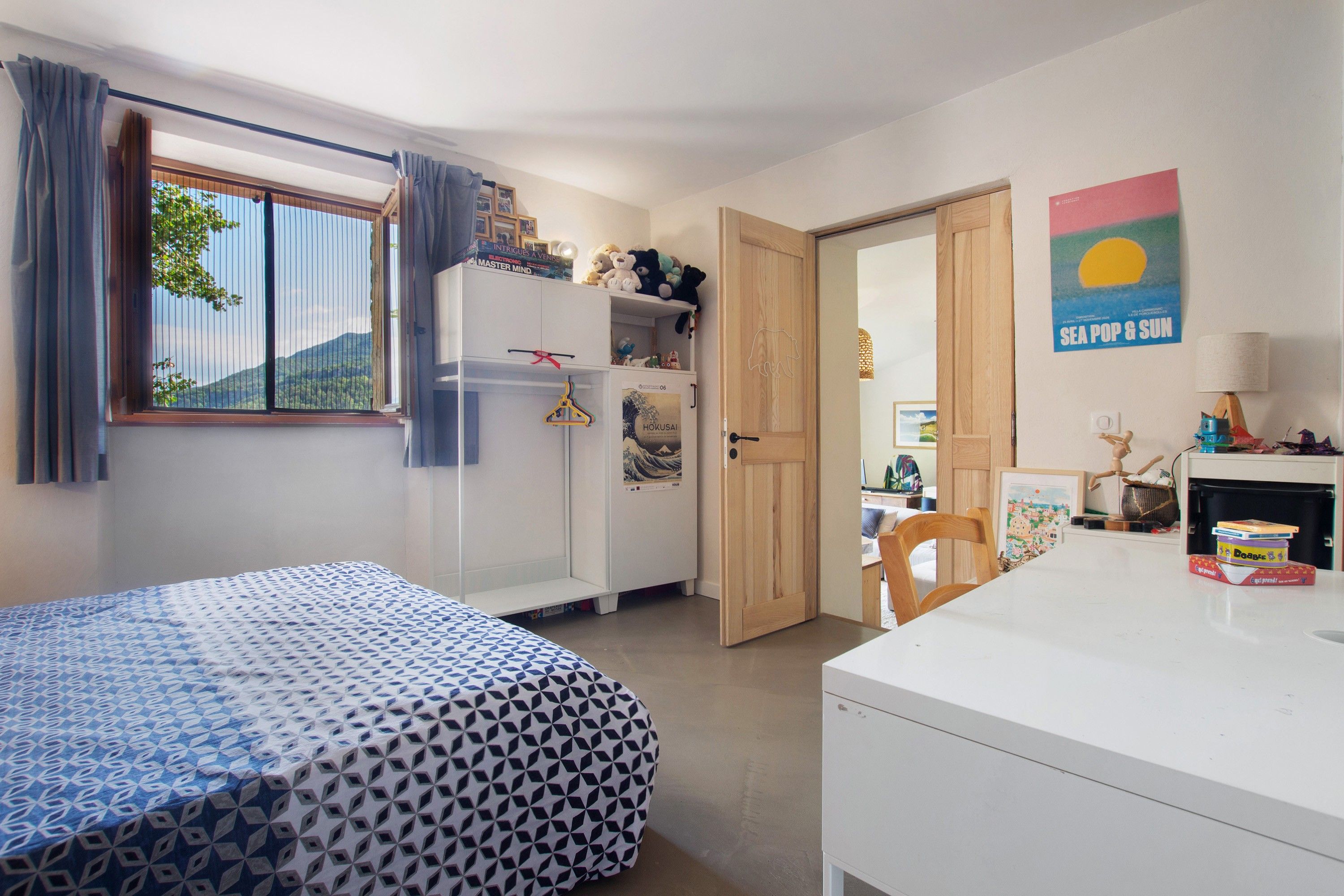 Een slaapkamer met een bed, een kledingkast, een bureau en een raam met gordijnen.