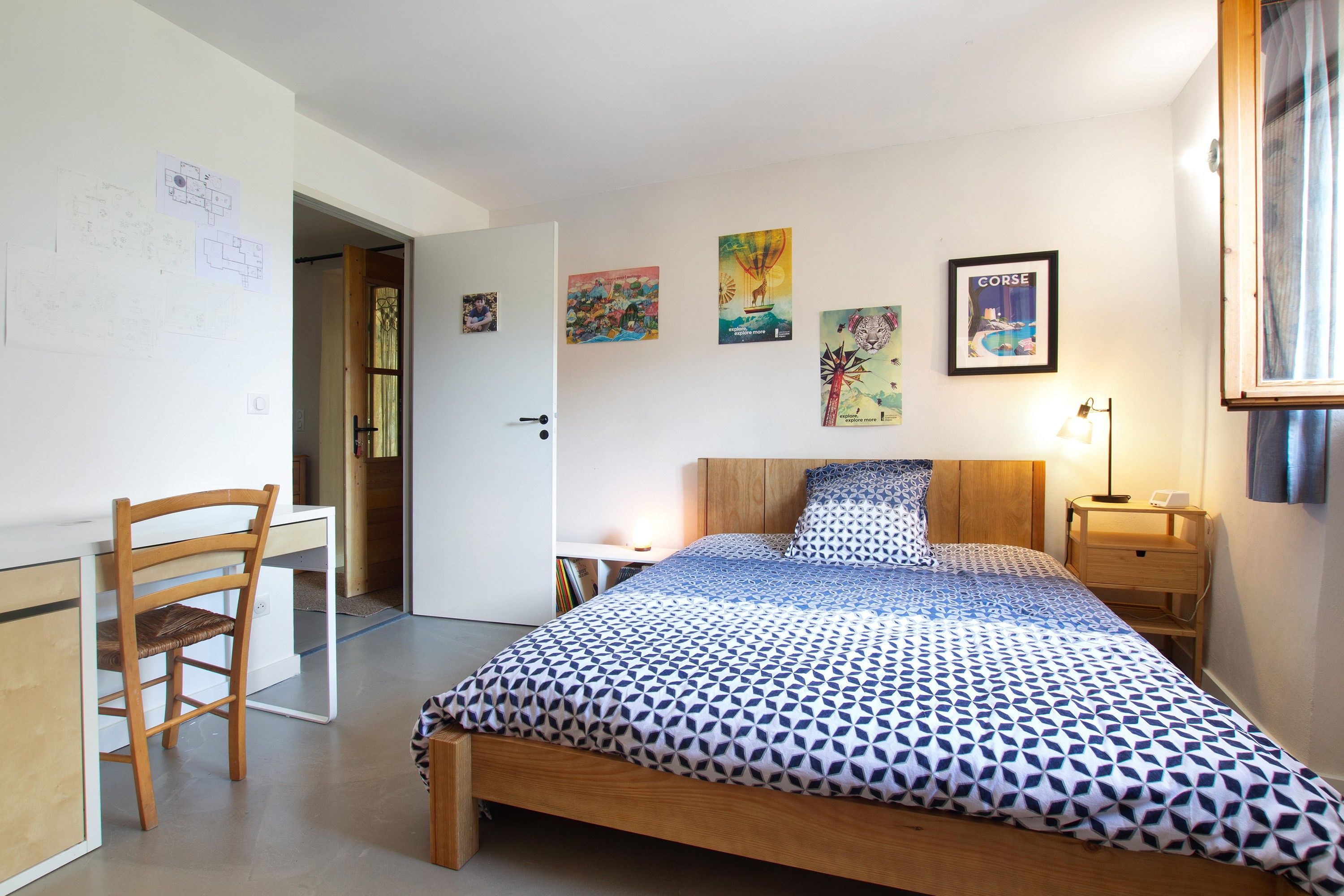 A bedroom with a bed, a chair, a bedside table, and a lamp.