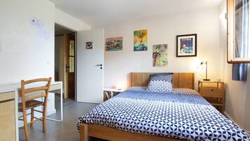 A bedroom with a bed, a chair, a bedside table, and a lamp.