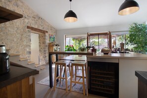 A kitchen with a stone wall, wooden bar stools, a wine rack, and pendant lighting.