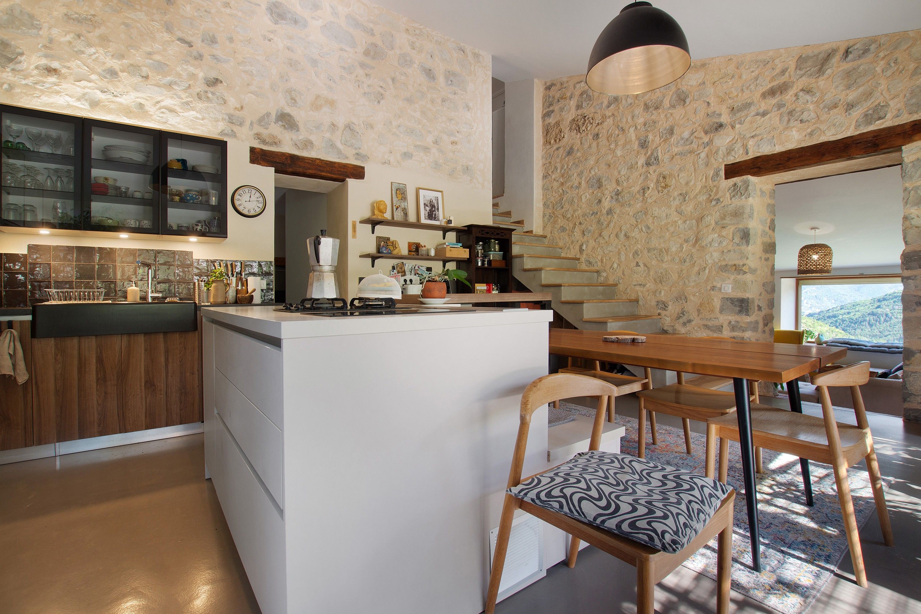 Una cucina moderna con isola centrale, sedie in legno e un muro in pietra.