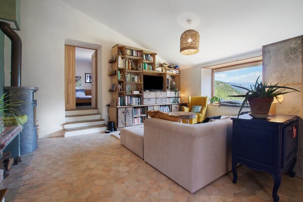 A cozy living room with a sofa, a bookshelf, a fireplace, and a view of the outdoors. - Country house 'La Bergerie du Grand Tilleul' with Mountain View, Private Garden, Wi-Fi (Val-de-Chalvagne)