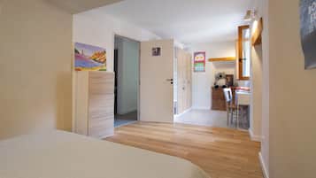 A room with a bed, a door leading to a kitchen, and a painting on the wall.