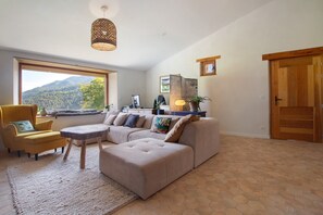 Una sala de estar con un ventanal grande, un conjunto de sofás, una silla, una mesita y una lámpara colgante.