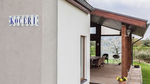 A covered outdoor area with a wooden deck, a table, chairs, and a barbecue grill.