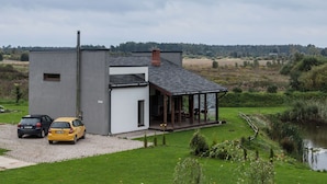 A modern two-story house with a covered porch, a gravel driveway, and a car parked in front.