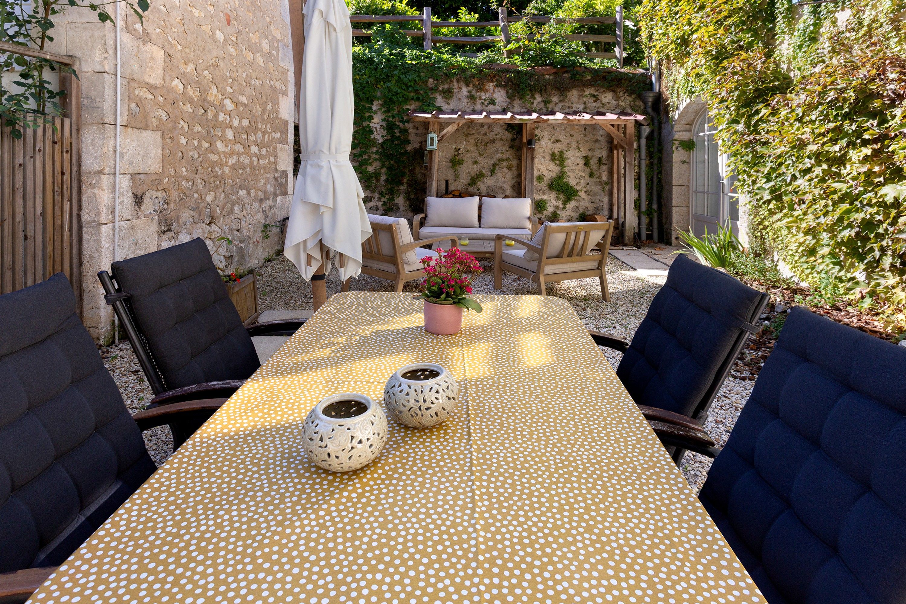 An outdoor patio with a table set for two, surrounded by chairs, and a small seating area with cushions.