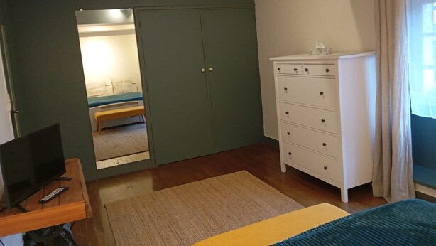 A bedroom with a bed, a dresser, a desk with a computer, and a mirror.