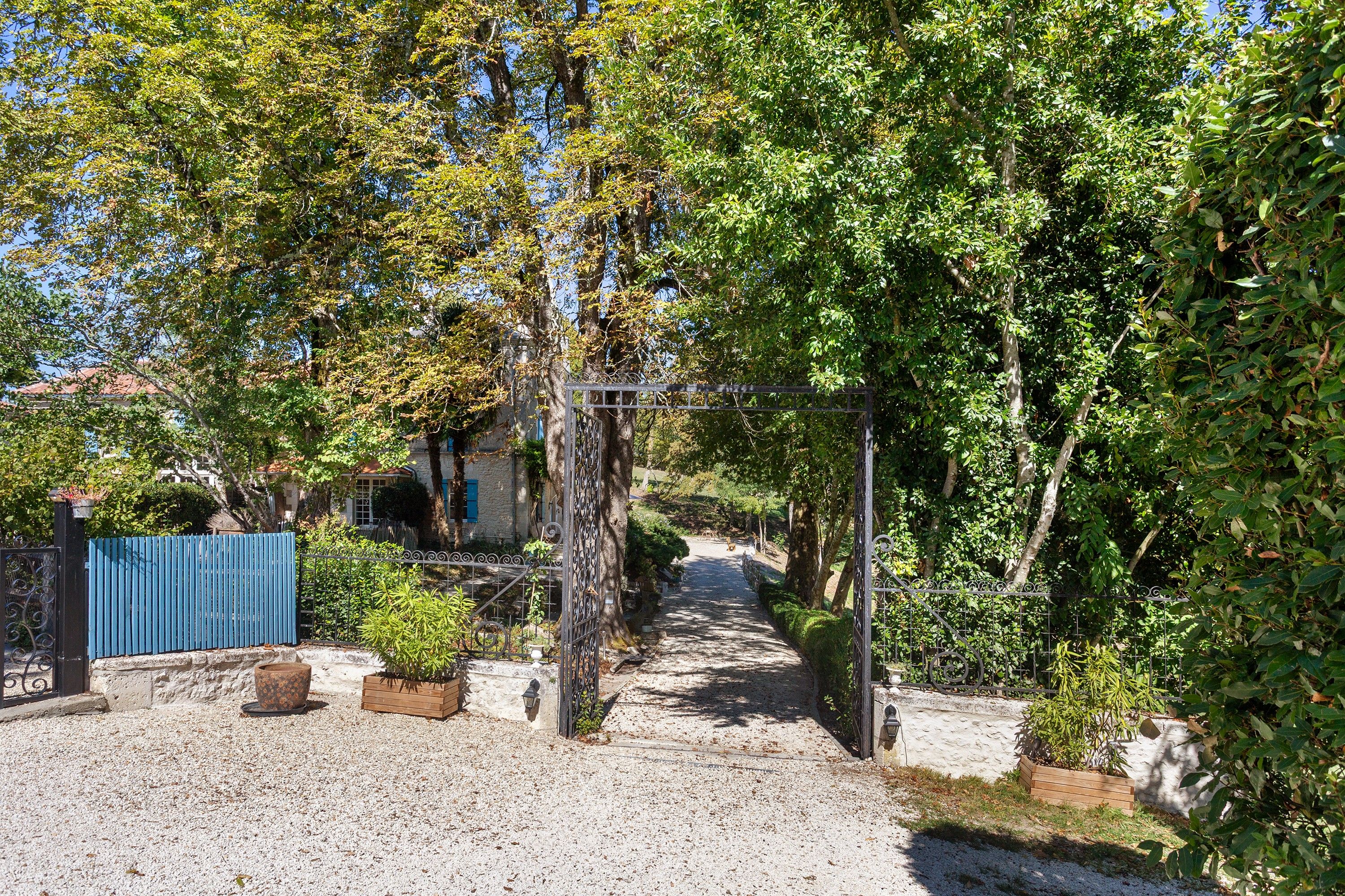 A gravel pathway leading to a house with a blue fence and a metal gate.