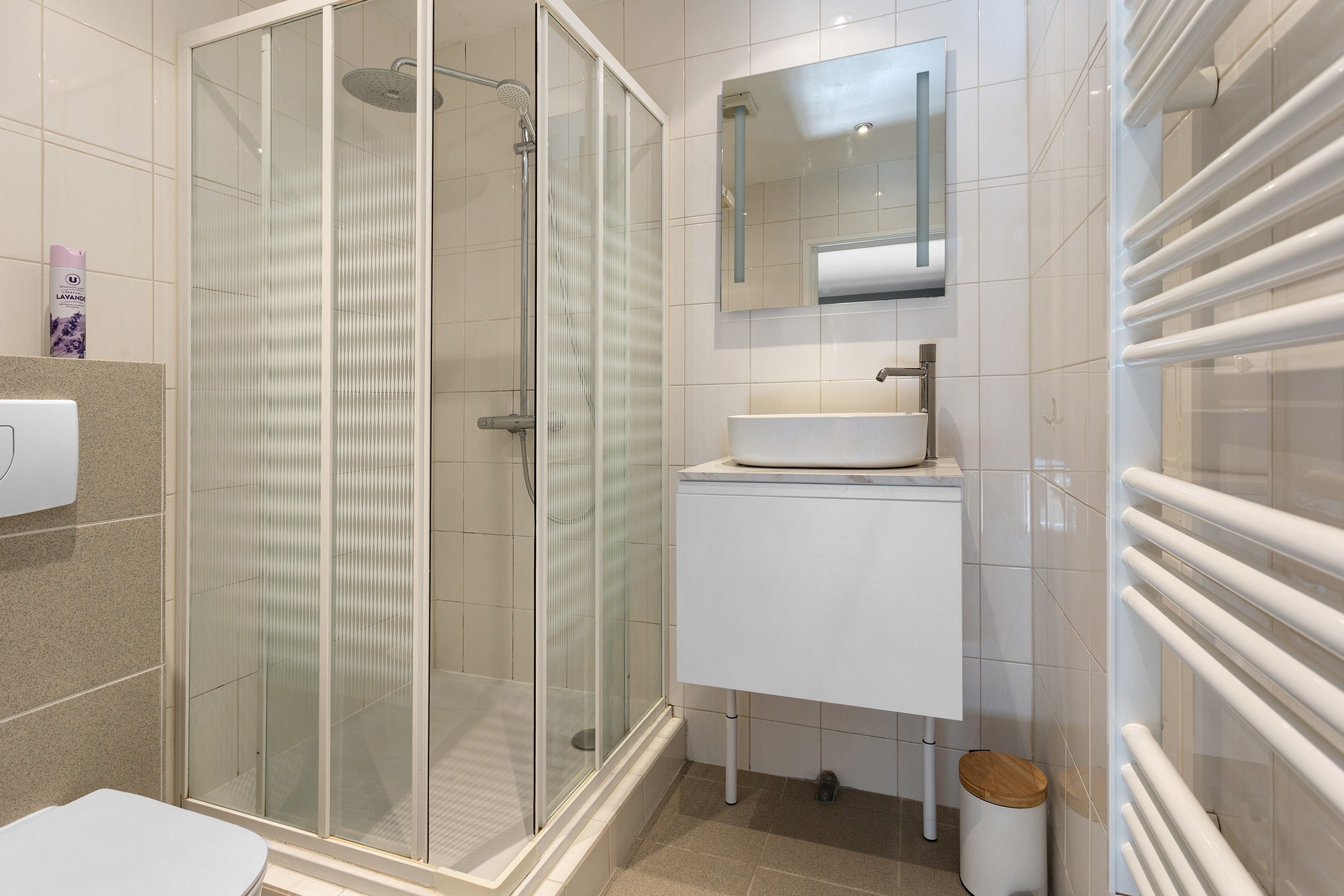 Een moderne badkamer met een douchecabine van glas, een witte wastafel en een spiegel erboven.