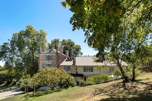 A two-story house with a tiled roof, surrounded by trees and a grassy area.
