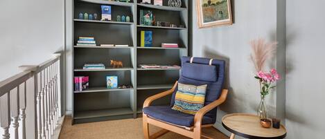 A corner room with a bookshelf, a chair, a small table with a vase, and a painting on the wall.