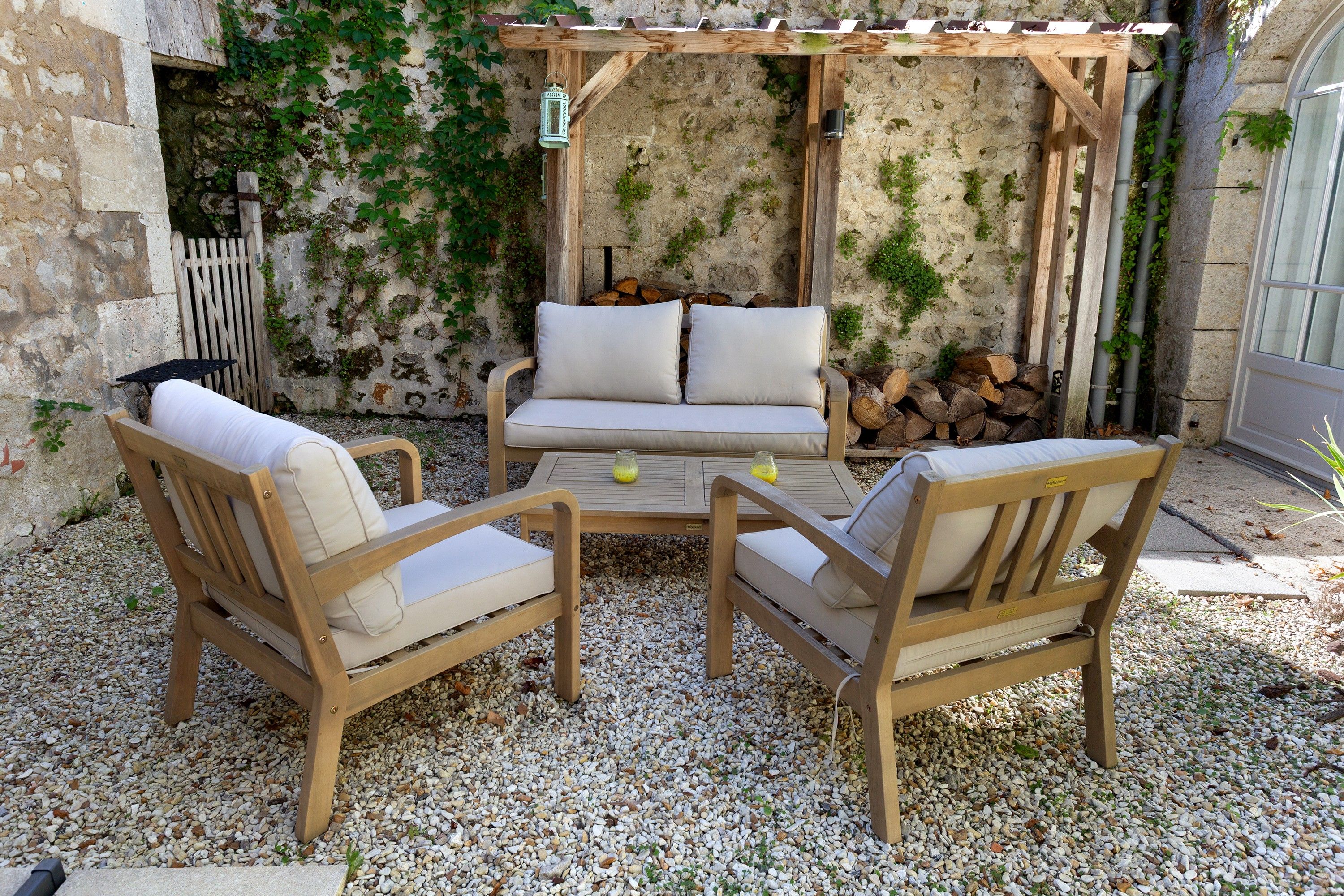 Een terras met twee houten stoelen en een bank, een houten tafel en een pergola.