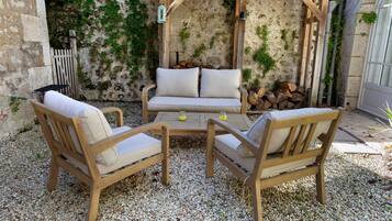 Een terras met twee houten stoelen en een bank, een houten tafel en een pergola.