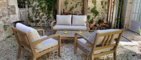 An outdoor seating area with two wooden chairs and a sofa, a wooden table, and a pergola structure.