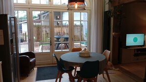 A dining area with a round table, chairs, a television, and a view through large windows.