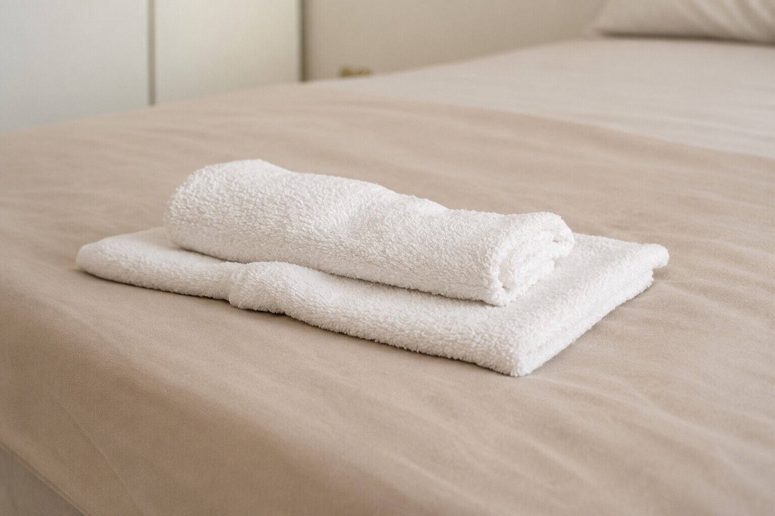 A neatly folded white towel on a beige bed with a pillow.