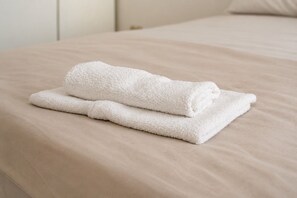 A neatly folded white towel on a beige bed with a pillow.