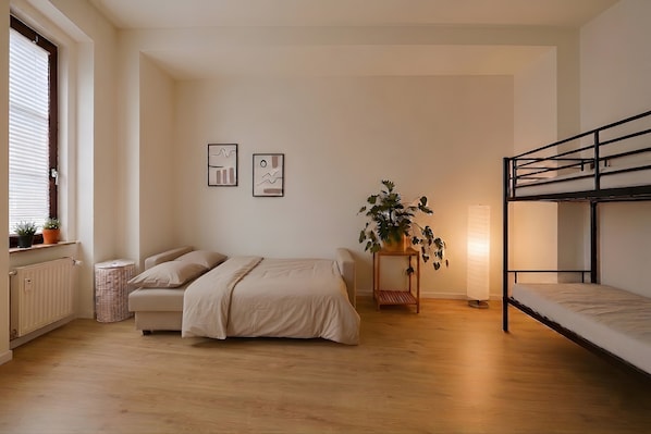 A bedroom with a bed, a bunk bed, a potted plant, and framed pictures on the wall.