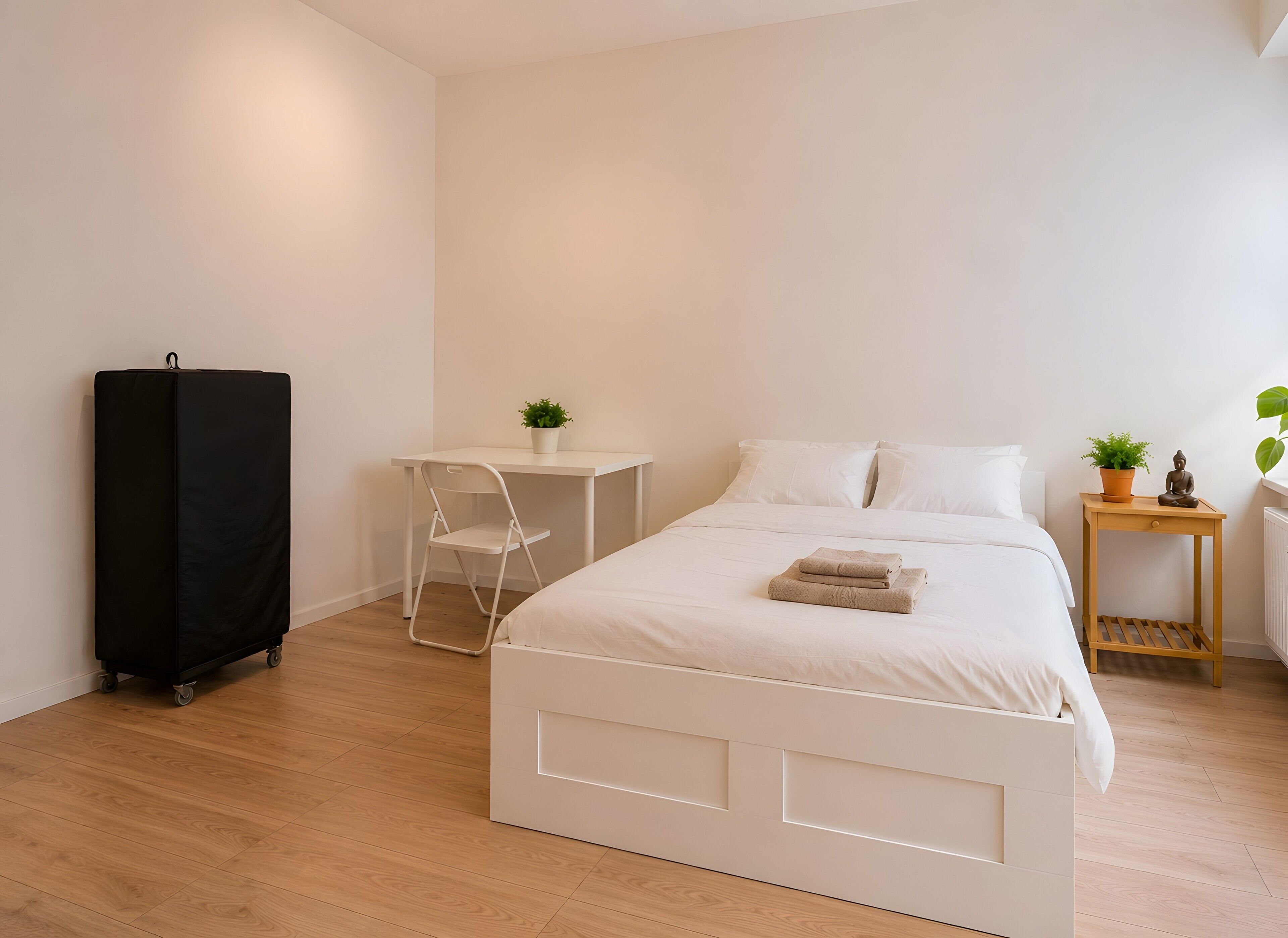 Ein schlicht eingerichtetes Schlafzimmer mit Bett, Schreibtisch, Stuhl, Kleiderschrank und einem kleinen Tisch mit Pflanzen.