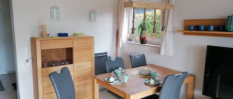 A dining area with a wooden table, chairs, a television, and a cabinet with glassware.