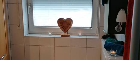 Pieni kylpyhuone, jossa on wc, ikkuna, jossa on sälekaihtimet, pyyhekoukku ja seinään kiinnitetty valaisin.