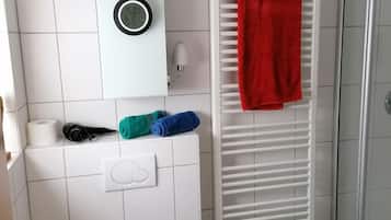 Une salle de bain comprenant des toilettes, un porte-serviettes avec une serviette rouge, un radiateur blanc et un espace douche.