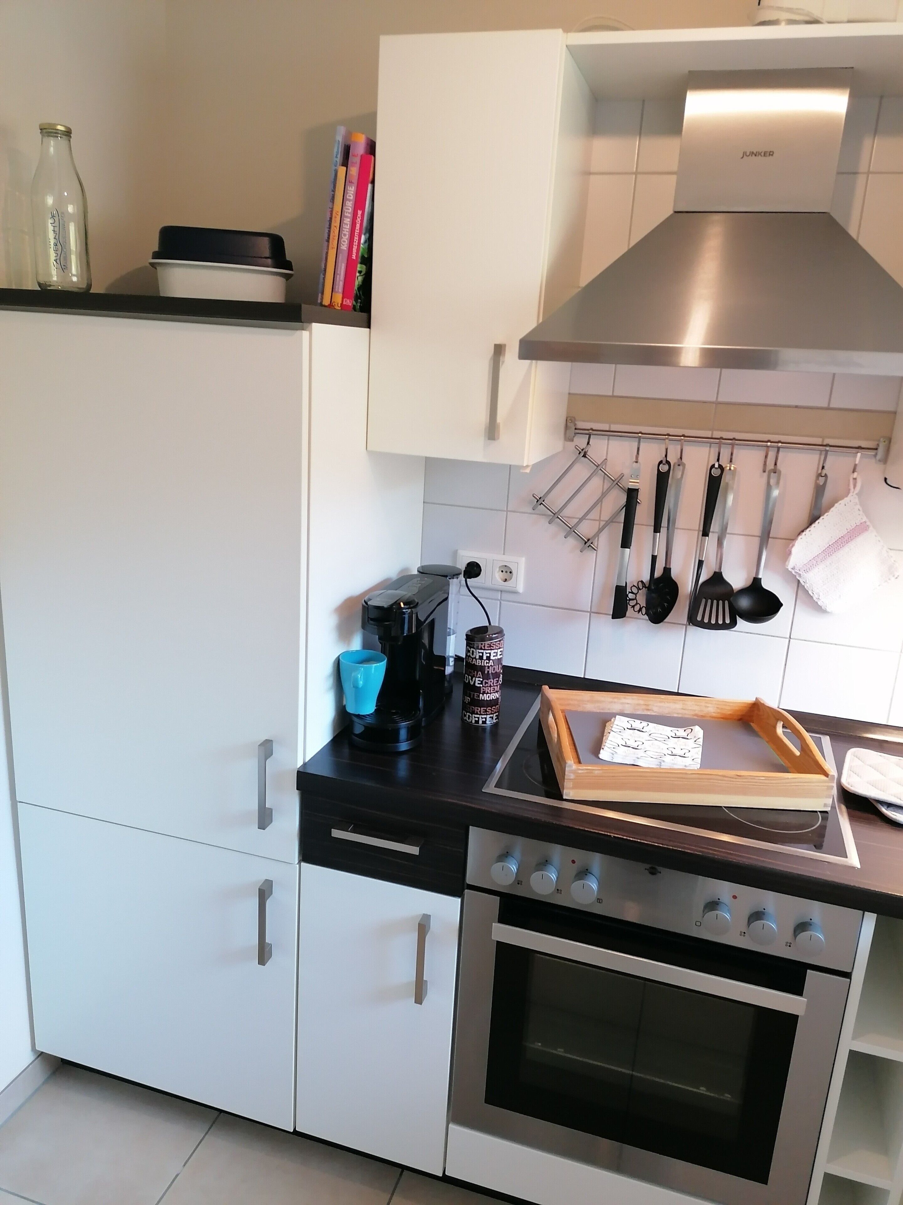 Eine kleine Küche mit weißen Schränken, einem Edelstahlbackofen und einer Kaffeemaschine auf der Arbeitsfläche.