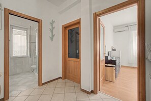 Un corridoio con una porta in legno che dà su un bagno, un armadietto in legno e un pavimento piastrellato.