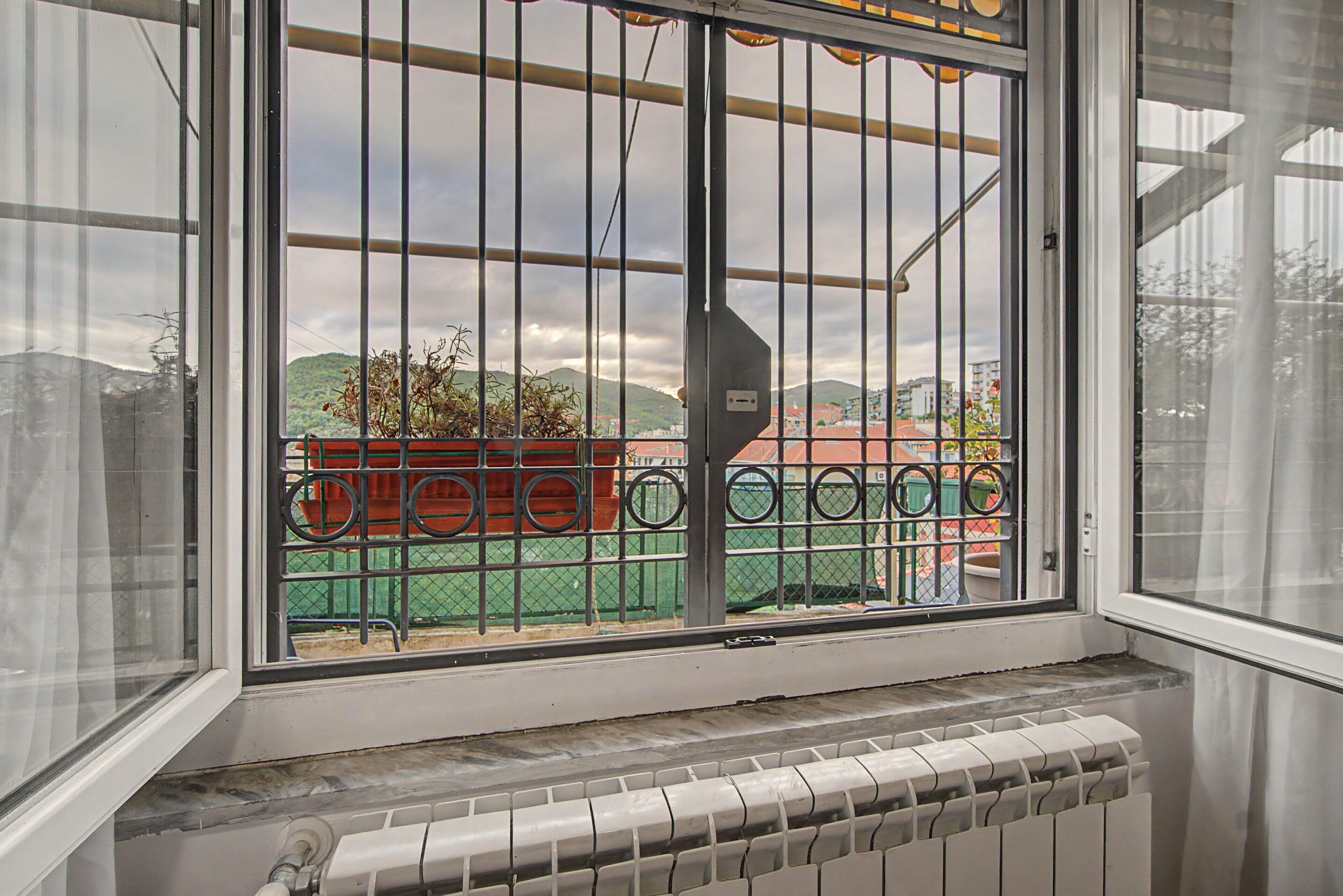 Una ventana con rejas y vistas a un edificio verde y colinas al fondo.