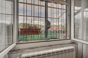 Une fenêtre avec des barreaux en métal, donnant sur un bâtiment vert et sur des collines en arrière-plan.