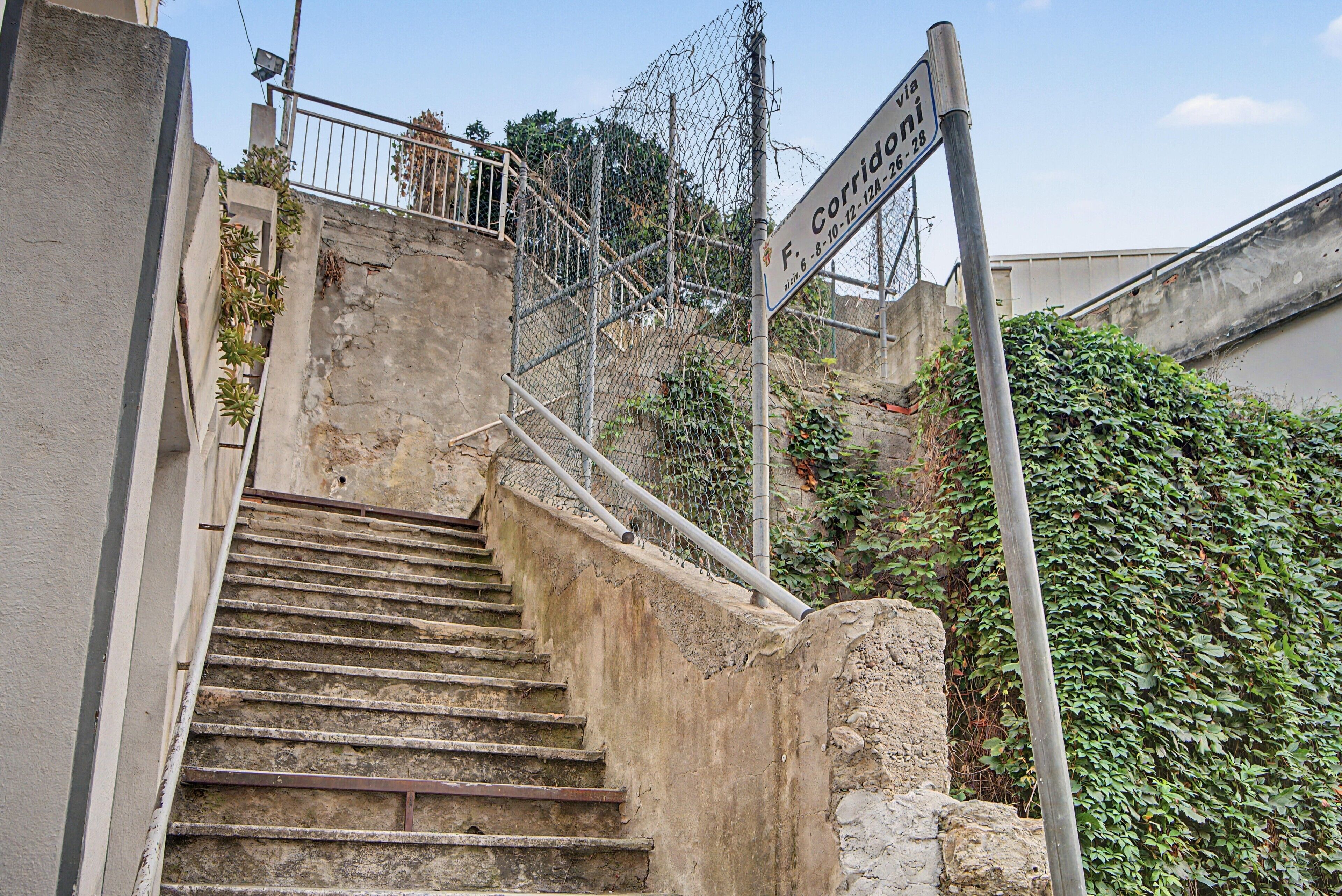 Una escalera de hormigón que sube hacia un edificio con una valla de metal y un cartel que indica un lugar.