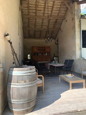 A rustic outdoor seating area with wooden furniture, a large barrel, and a bookshelf.