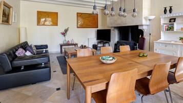 Een ruime woonkamer met een grote houten eettafel, zittende meubels, een open haard en decoratieve muurkunst.