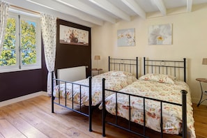Un dormitorio con una cama doble, un radiador, una ventana con cortinas y decoración floral en las paredes.