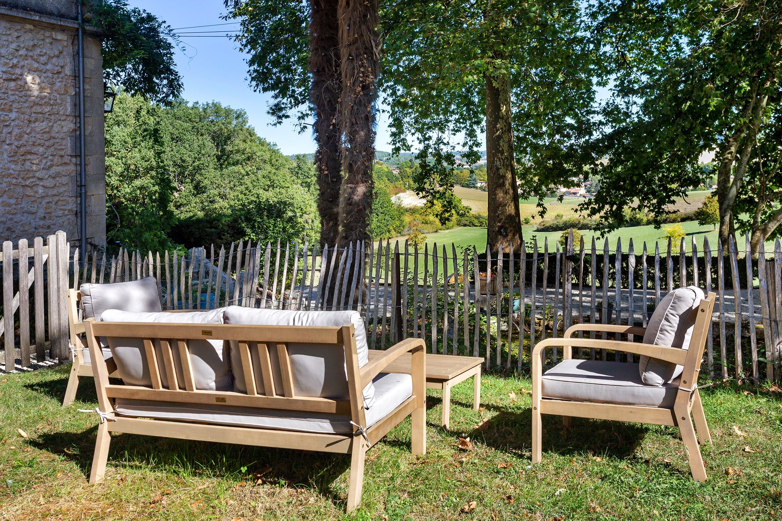 Een terras met een houten bank en stoel, omringd door een houten omheining en bomen.