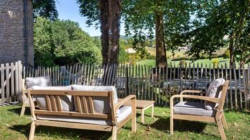Een terras met een houten bank en stoel, omringd door een houten omheining en bomen.