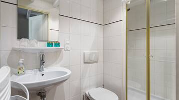 Une salle de bain avec un lavabo blanc, un miroir et des toilettes, une douche en verre et un mur recouvert de carreaux blancs.